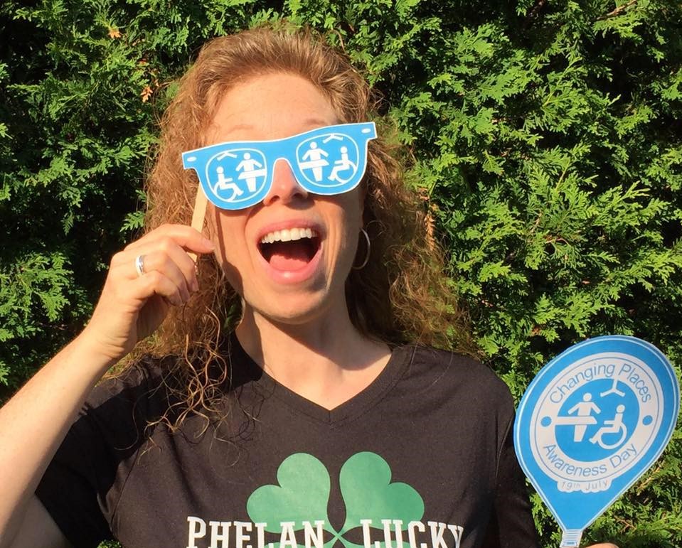 Stephanie Lecler with a big smile holding paper eye glasses with Changing Places logo on them